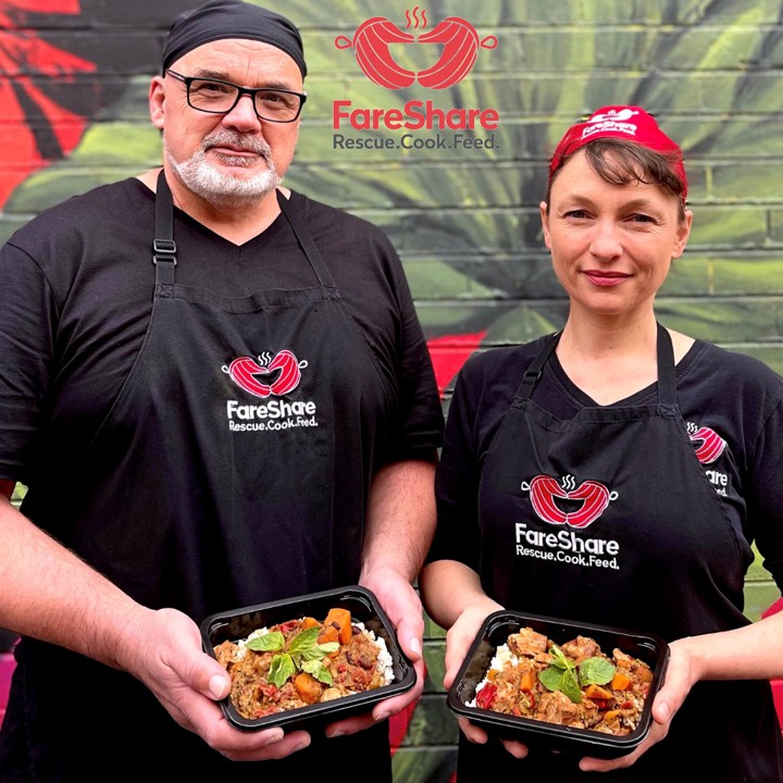 Two people in aprons holding bowls of tasty looking food