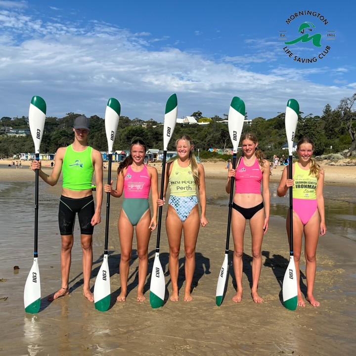 People in bright bathers standing at the beach with paddles