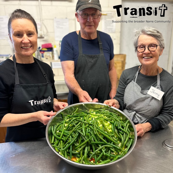 3 people in aprons smiling holding a big bowl of vegetables