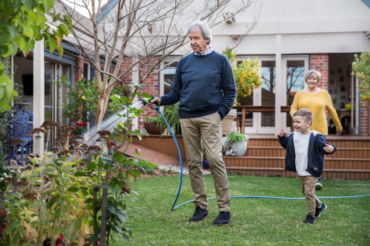 Man watering the garden with child running