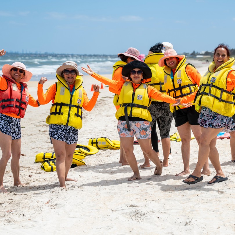 A group of happy smiling women at the beach wearing life jackets.