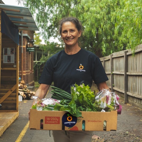Smiling lady holding a box of fresh vegetables.