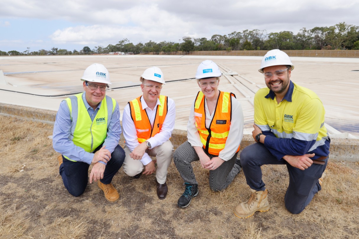People in high vis vests kneeing in from of the water storage basin. 