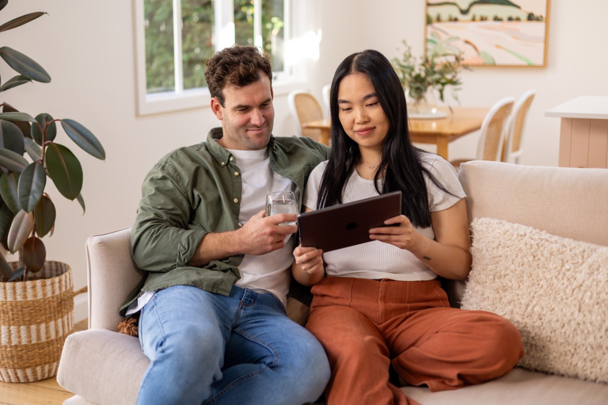 Two people sitting on a couch looking at a tablet.