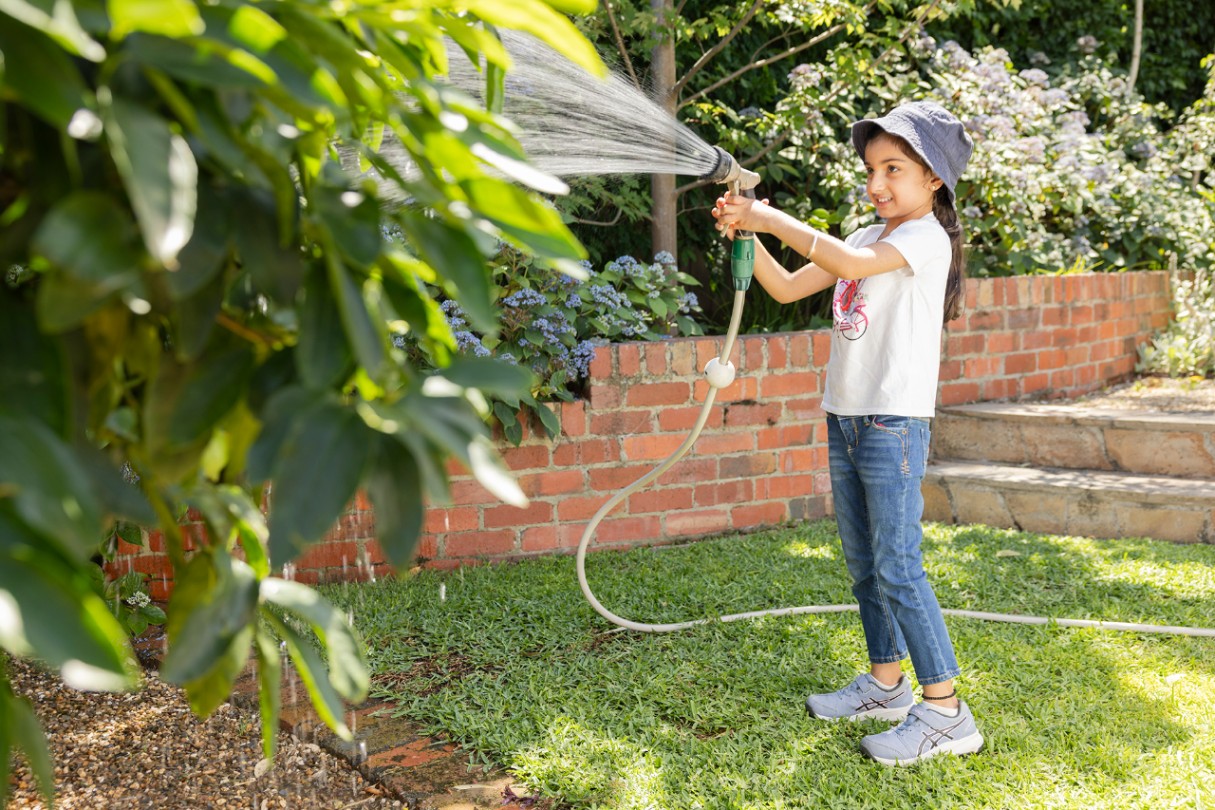 Child wearing a hat watering a tree.
